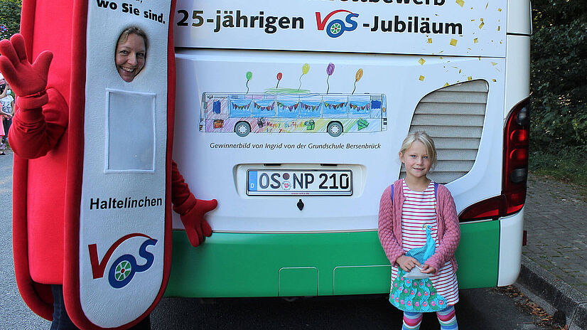 Malwettbewerbgewinnerin Ingrid steht vor ihrem Bild am Heck eines Busses.