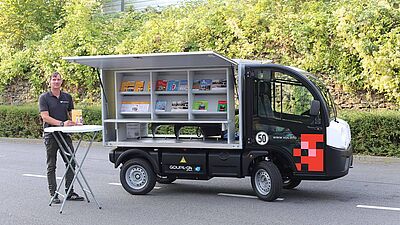 Ein Mobilitätsberater steht neben dem V O S Infomobil mit aufgeklappter Seitenwand und zeigt ein Informationsblatt.