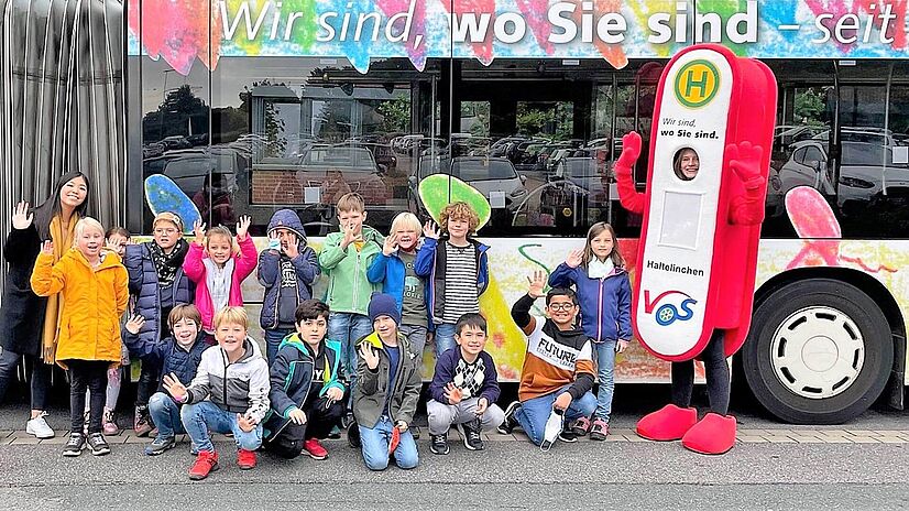 Malwettbewerb Grundschüler vor Bus mit VOS Maskottchen Haltelinchen.