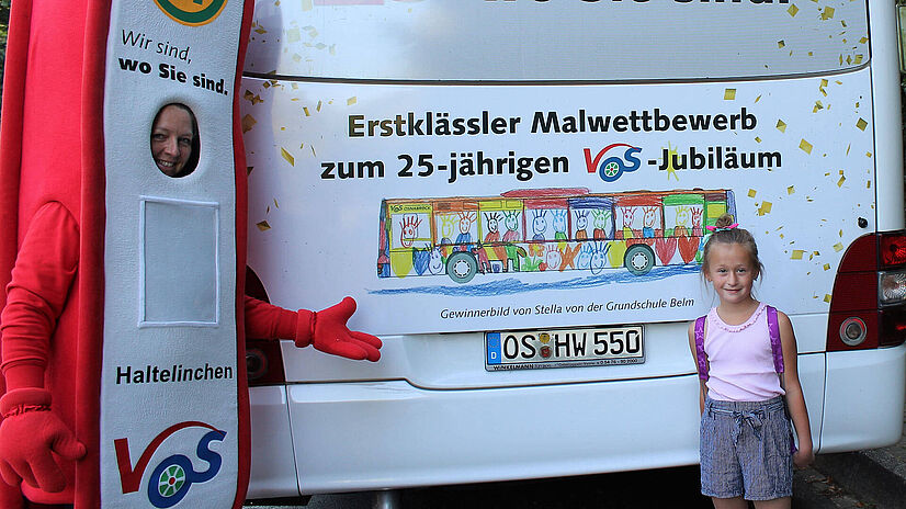 Malwettbewerbgewinnerin Stella steht vor ihrem Bild am Heck eines Busses.