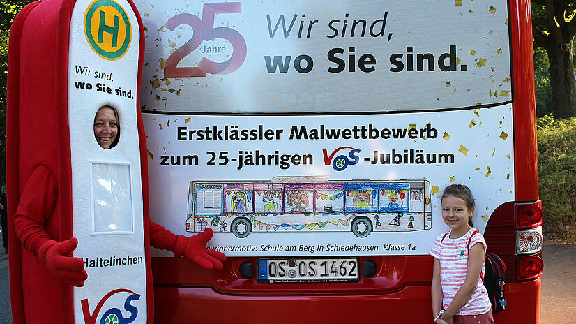 Malwettbewerbgewinnerin Emily steht vor ihrem Bild am Heck eines Busses.