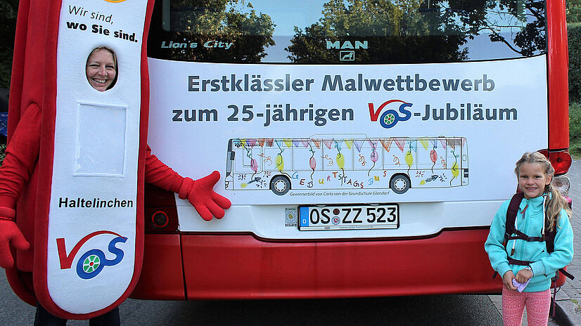 Malwettbewerbgewinnerin Carla steht vor ihrem Bild am Heck eines Busses.