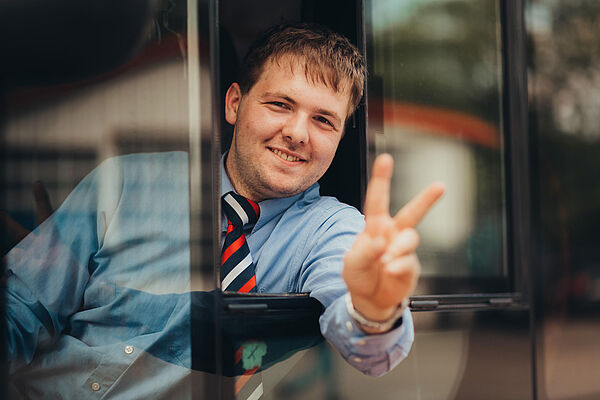 Busfahrer-Azubi zeigt aus dem Seitenfenster des Busfahrerplatzes das Victory-Zeichen.