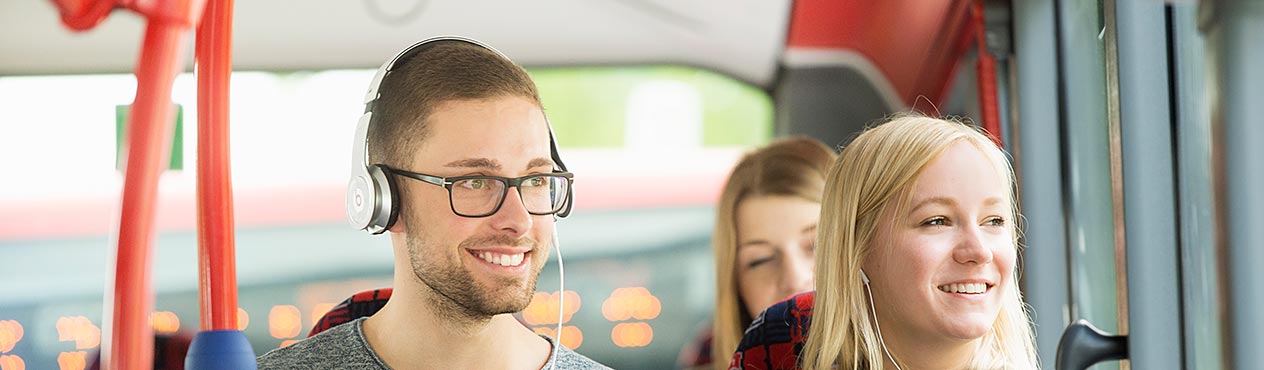 Lächelnde, junge Menschen mit Kopfhörern im Bus